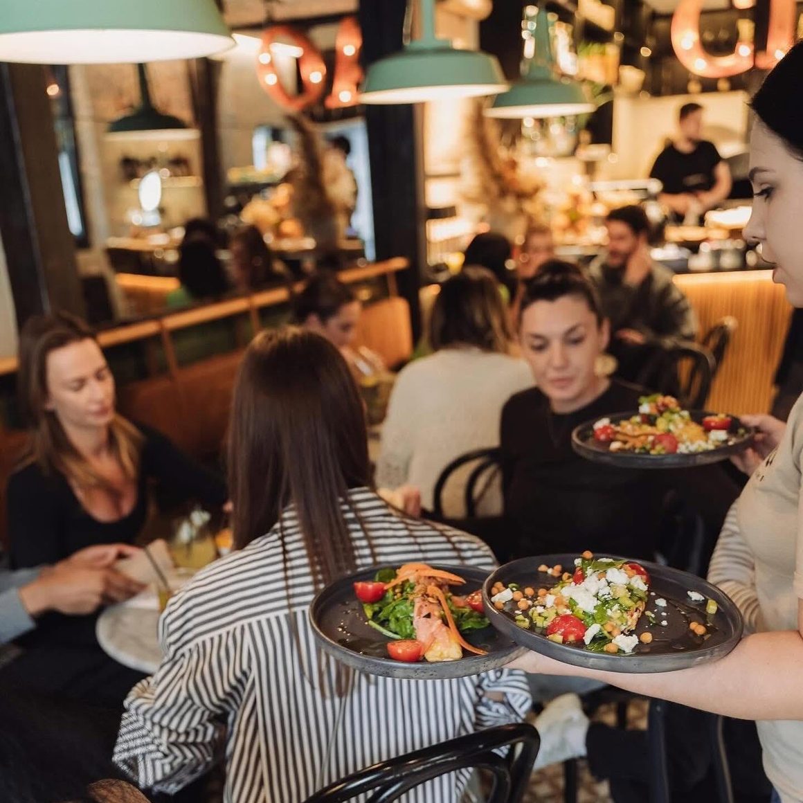 Interiorul restaurantului Mano+Bocca la ora prânzului, cu farfurii cu somon și salată de năut duse la masă