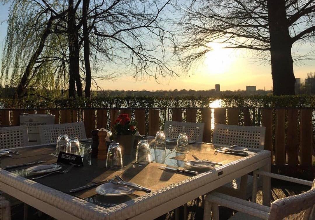 masa alba cu farfurii si pahare, iar in fundal copaci si lacul herastrau, fotografiata la apus, la restaurant La Brasserie Bistr&Lounge, unul din restaurante franțuzești din București