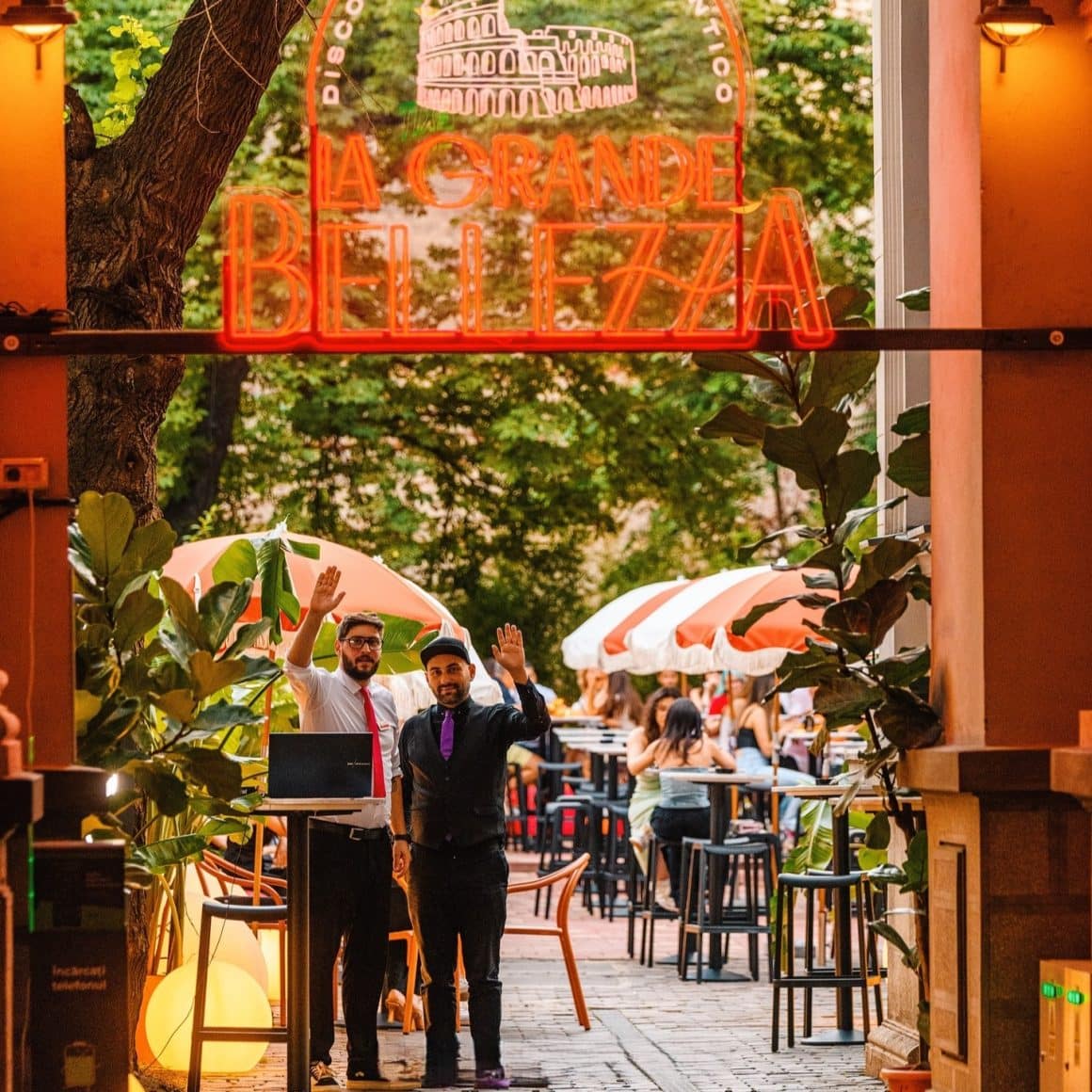 Intrarea în terasa La Grande Bellezza din București, cu zone de dining în aer liber și umbrele roșu-alb.