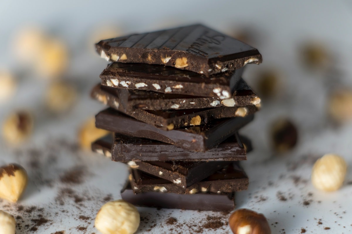 bucati de ciocolata neagra cu alune, suprapuse, aliment care combate anxietatea in padenmia de COVID-19