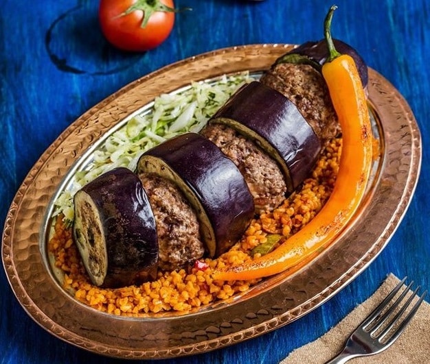 close up din restaurant efes turkish cuisine concept, cu un platou de paltican kebab, cu vinete umplute cu carne tocate, servite cu salata si ardei iute, platou fotografiat pe fundal albastru