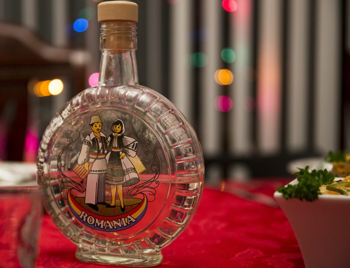 sticlă de tuica rotunda, transparenta , cu un barbat si o femeie desentai pe sticla, in costume traditionale românești - imagine reprezentativă pentru băuturi românești tradiționake - țuică și palincă