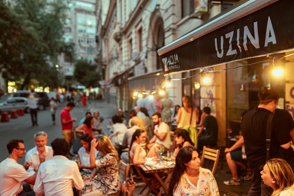 mai mulți tineri socializează la mesele de la intrarea intr-una dintre prăjitoriile de cafea din București