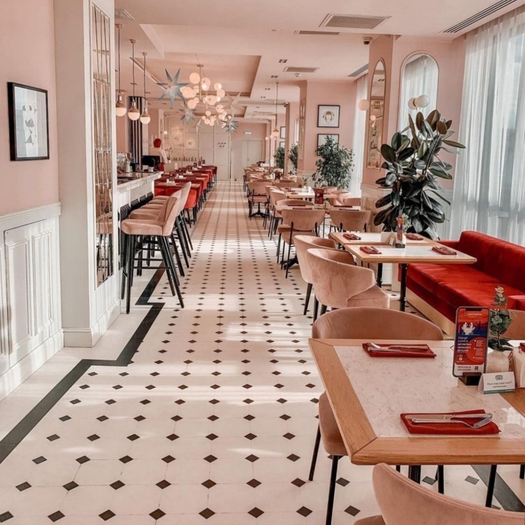 nterior Cișmigiu Bistro la Etaj București, cu podea mozaic alb-negru, scaune roz și canapele roșii din catifea, bar lateral și corpuri de iluminat suspendate