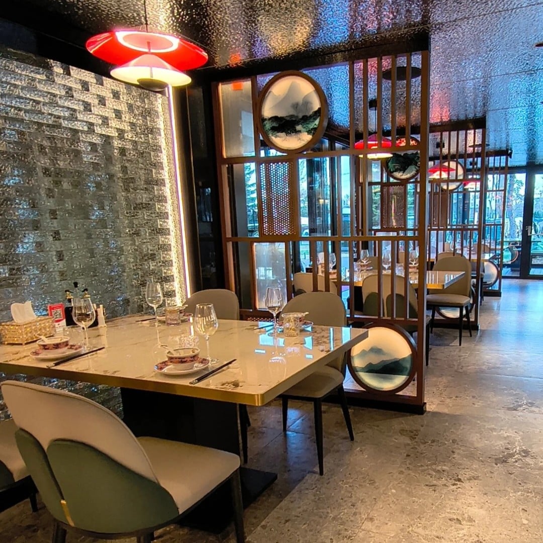 Interior Shuyu restaurant chinezesc București Herăstrău, cu mese din marmură, scaune verzi, lampi roșii suspendate și separatoare din lemn cu tablouri rotunde în stil asiatic