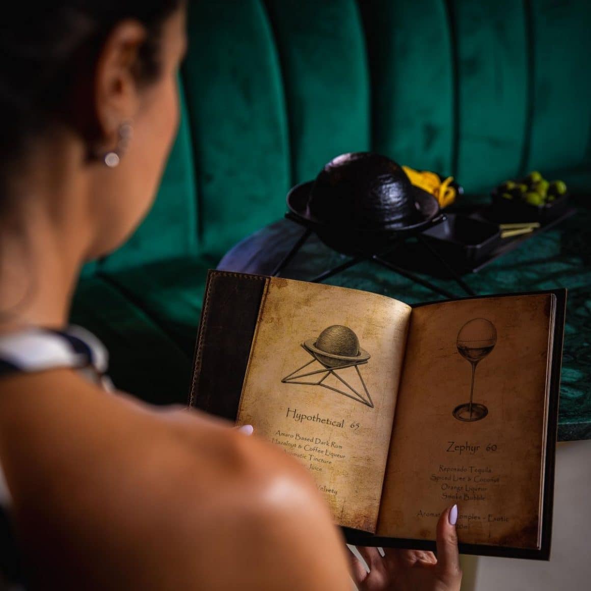 Femeie citind meniul de cocktailuri la Sous Sol București, bar subteran cu canapele verzi de catifea și cocktailuri de autor, un loc intim pentru o seară între prietene de restaurante 8 martie