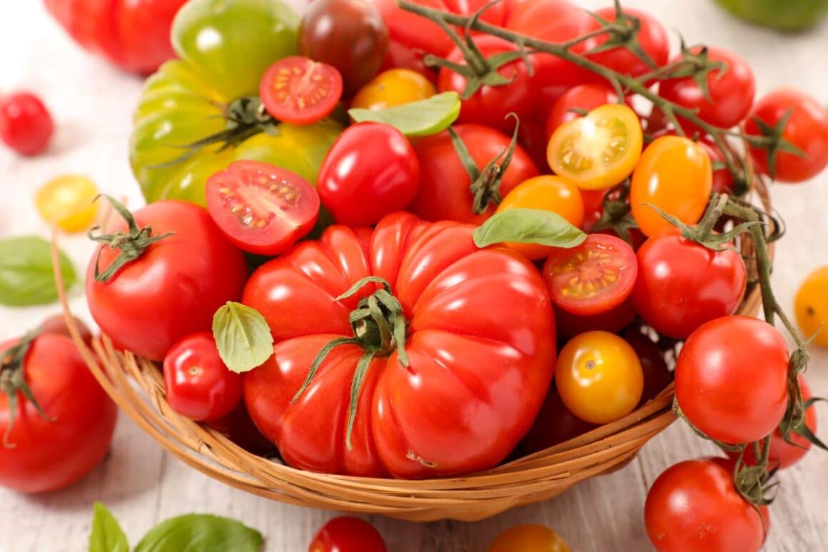 diferite tipuri de tomate așezate într-un coș de răchită pe o masă de lemn