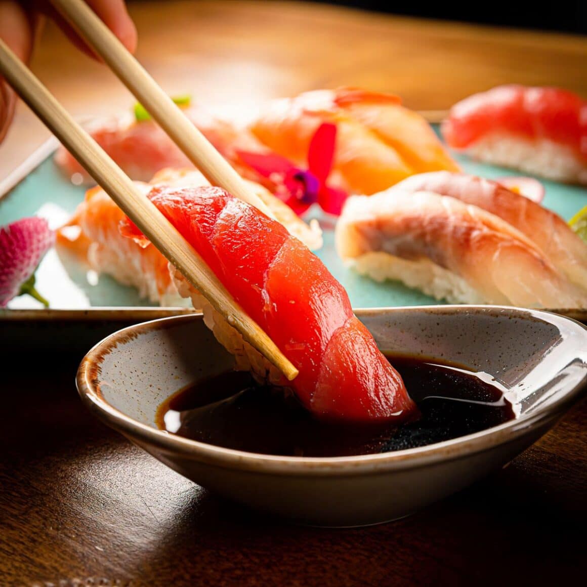 o bucată de sushi cu somon este înmuiată în sos de soia cu bețișoare chinezești - gust umami