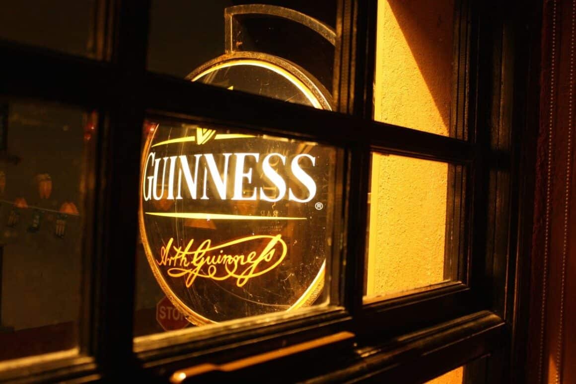 o caseta luminoasa rotunda cu Guinness este fotografiata pe geam, din interiorul unui pub 