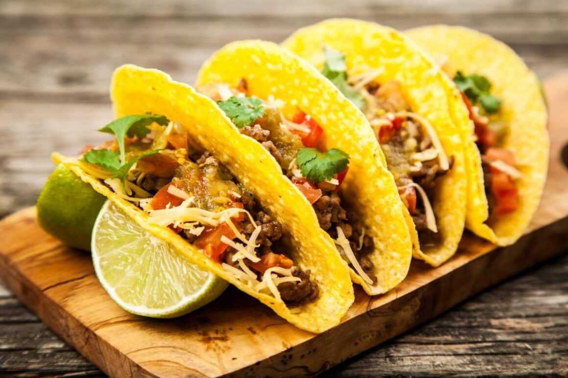 patru tacos sunt asezati intr-un suport, alături de cateva felii de lime