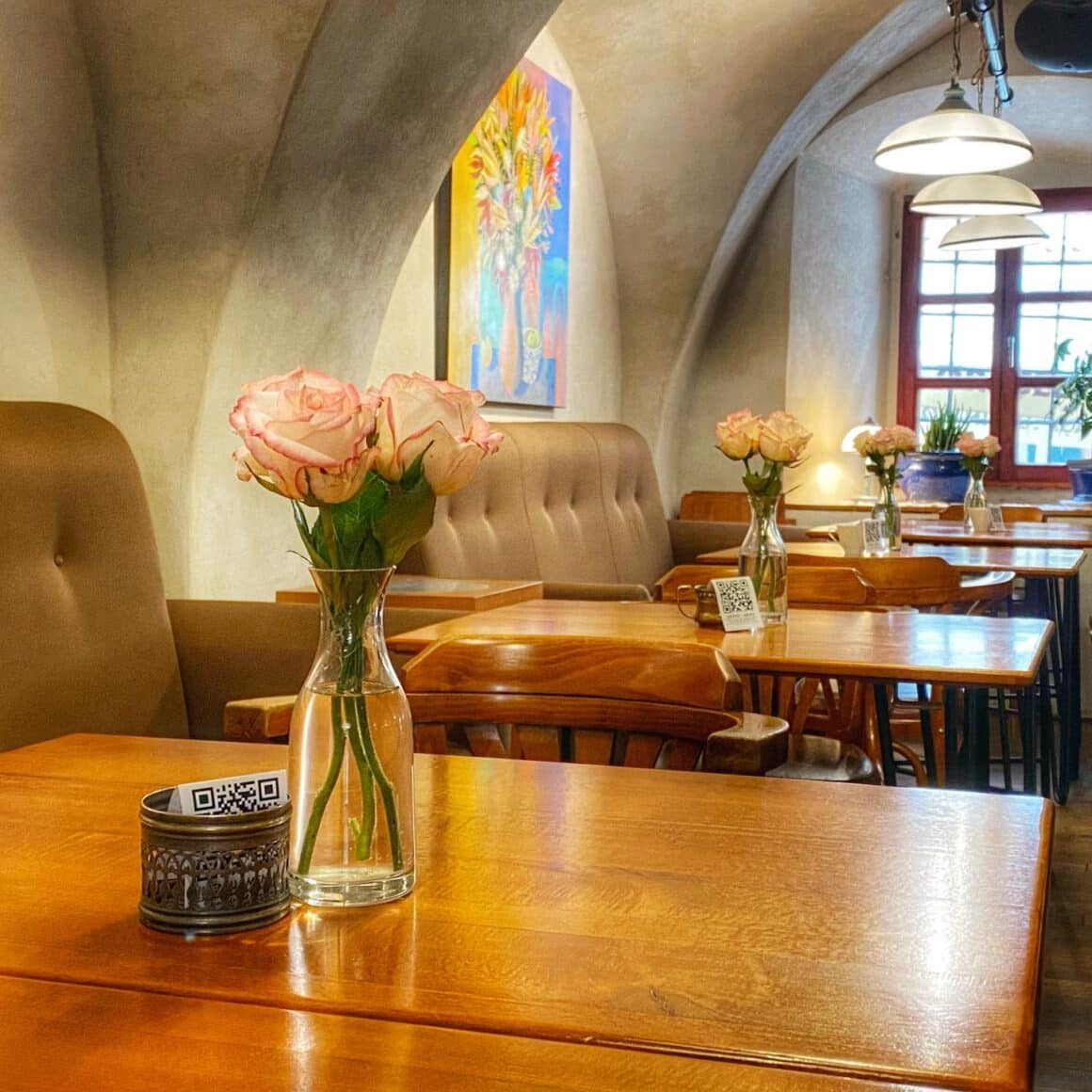 vaza cu trandafiri asezata pe masa la restaurant Bistro de Lasrte, iar in fundal tavanul boltit si o fereastra catre strada