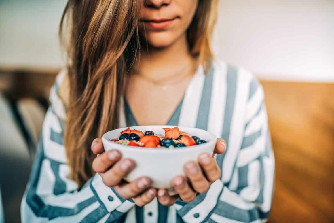 Imagine crop cu o femeie care tine in maini un bol de cereale cu fructe de padure, pentru micul dejun