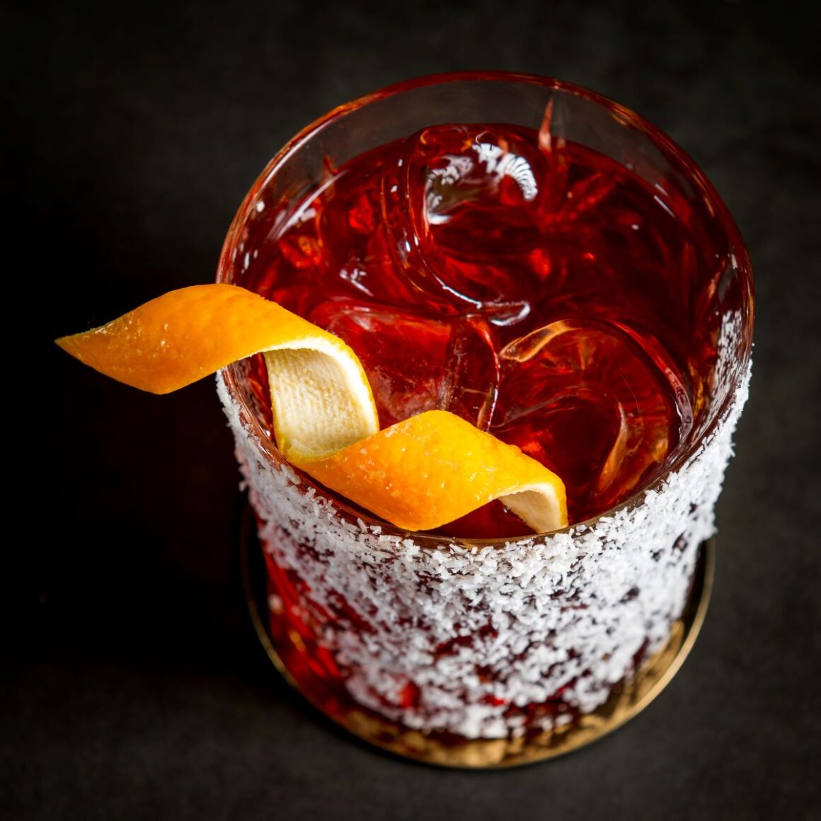 un pahar de sticla cu un cocktail negroni , decorat cu o coaja de portocala răsucita