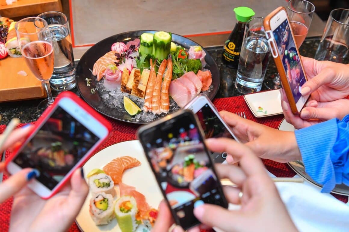 oameni care fotografiaza cu telefoanele niste farfurii cu preparate japoneze