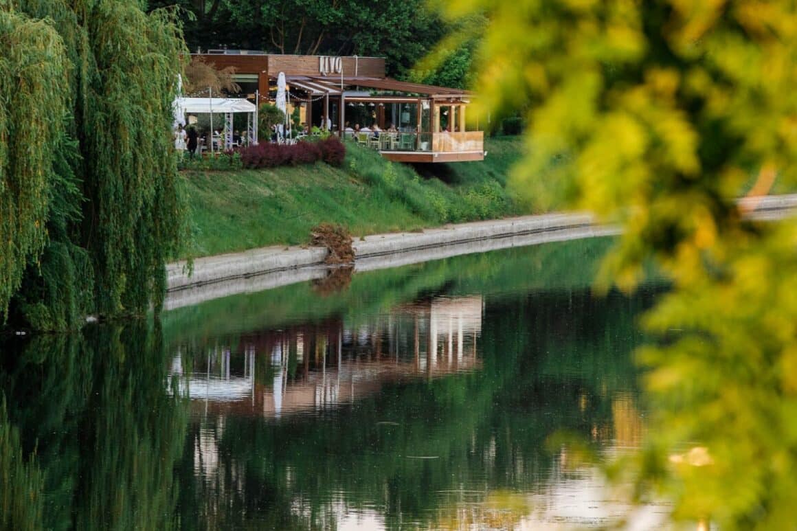 Restaurant Rivo fotografiat de la distanta, aflat pe malul lacului, inconjurat de copaci si verdeata- unul din restaurante bune din Oradea