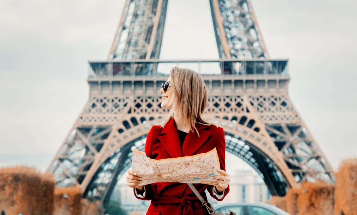 femeie in haina rosie cu o harta in mana, fotografiata in fata Turnului Eiffel. Imagine concept pentru c[l[torie la Paris. Restaurante din Paris