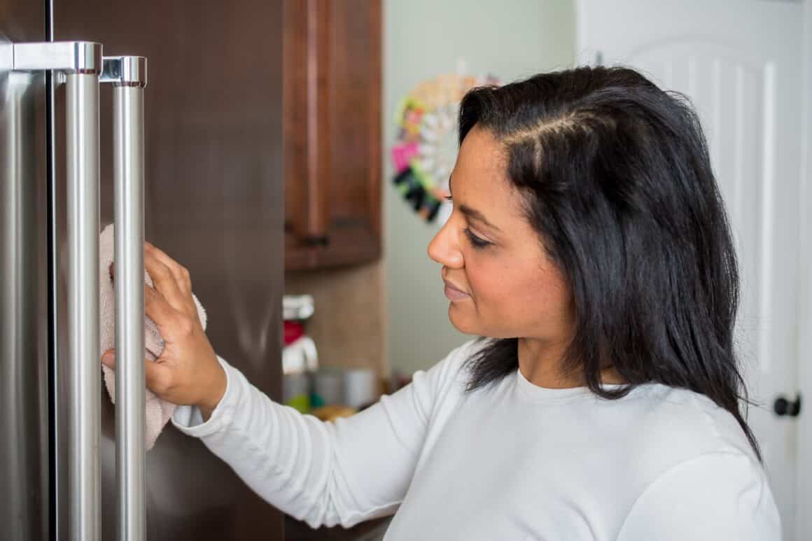 Femeie care curata frigiderul din otel inoxidabil cu produse de curățenie naturale