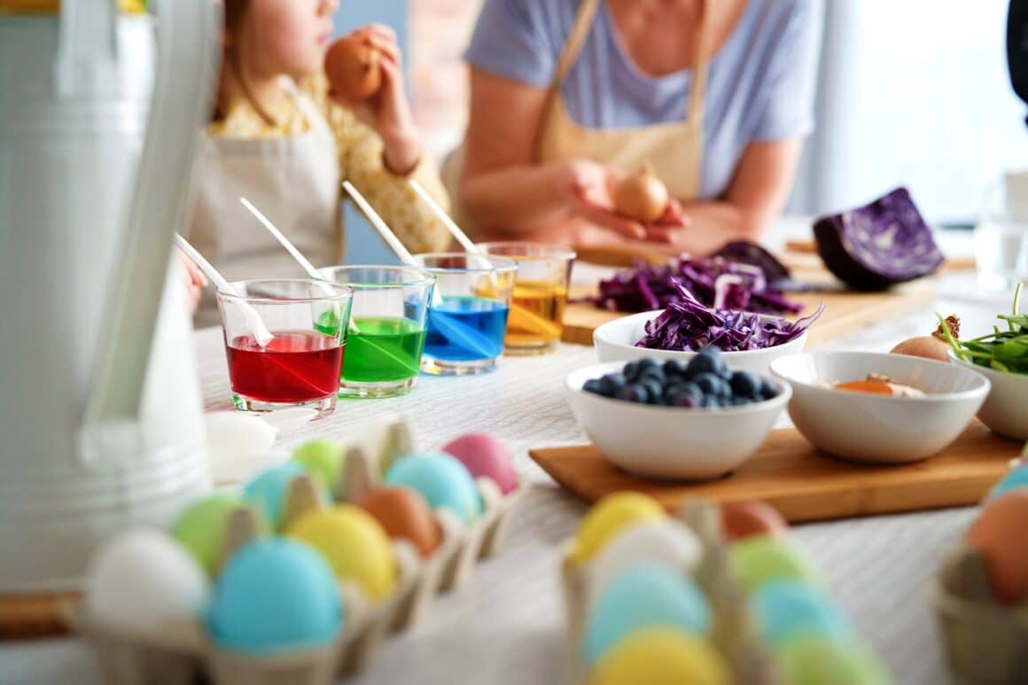 close up cu o masa pe care stau oaă vopsite natural, alaturi de boluri cu diverse ingrediente, pahare cu vopsea in ele, iar in fundal mama si fiica