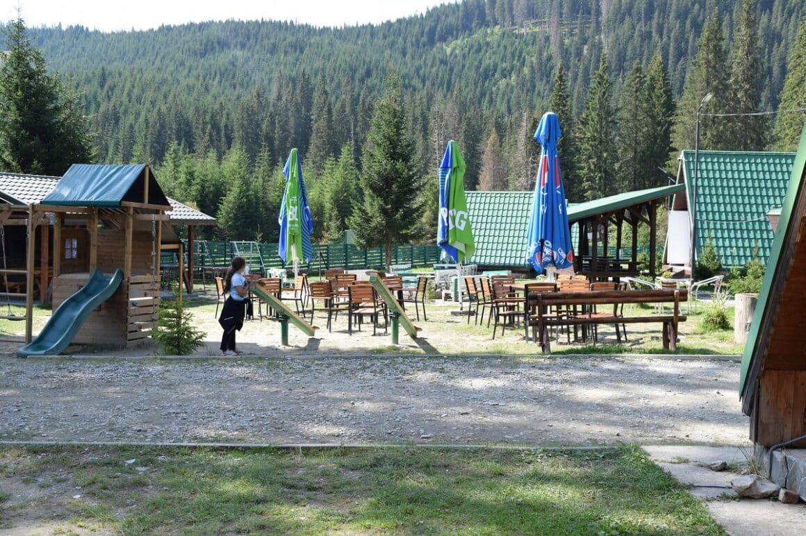 Zona de luat masa de la Camping Zanoaga, cu multe mese si scaune si locuri de joaca pentru copii.