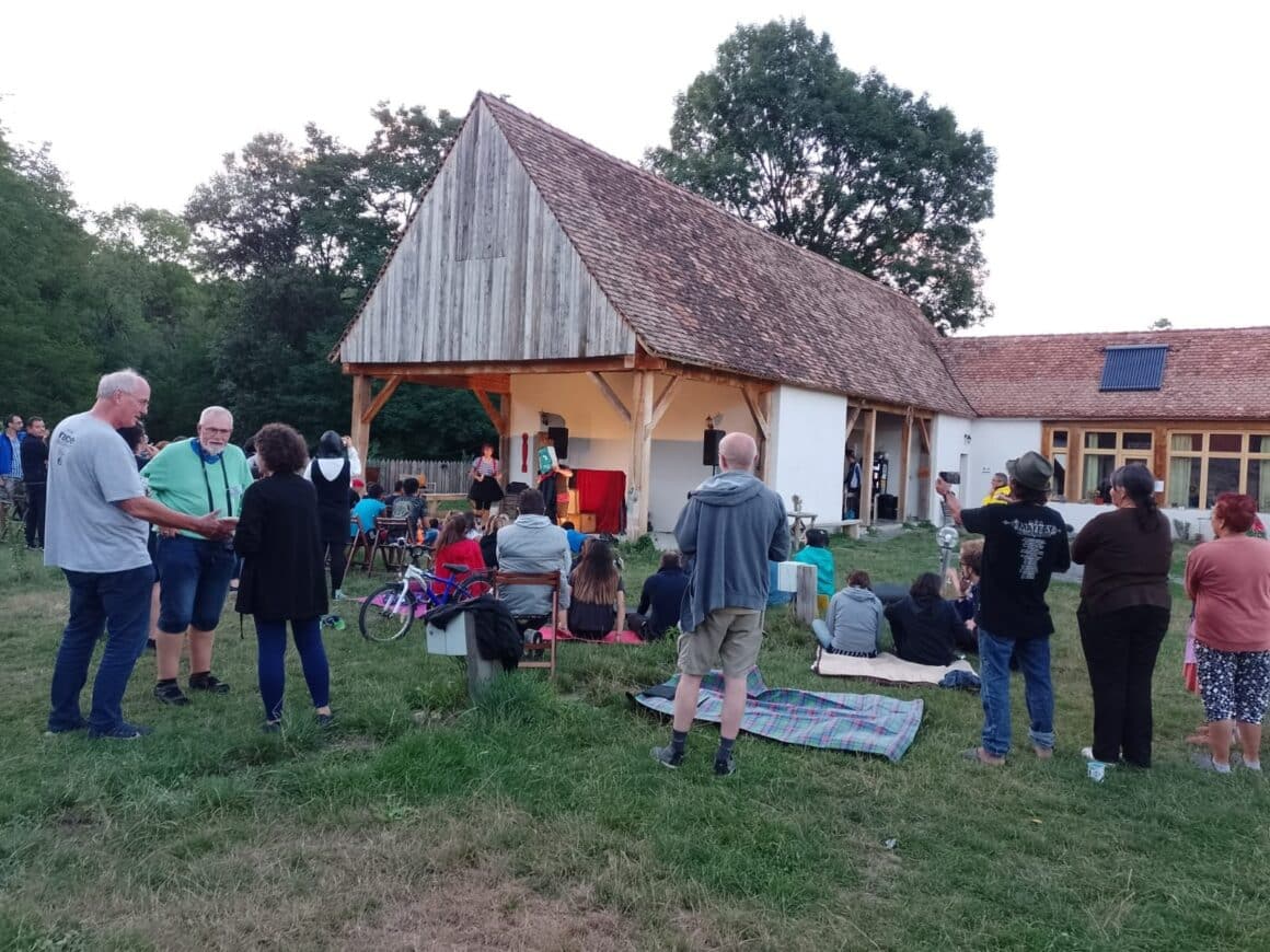 Curte plina de oameni care stau de vorba pe iarba in fata unei case satesti la Camping ZOri