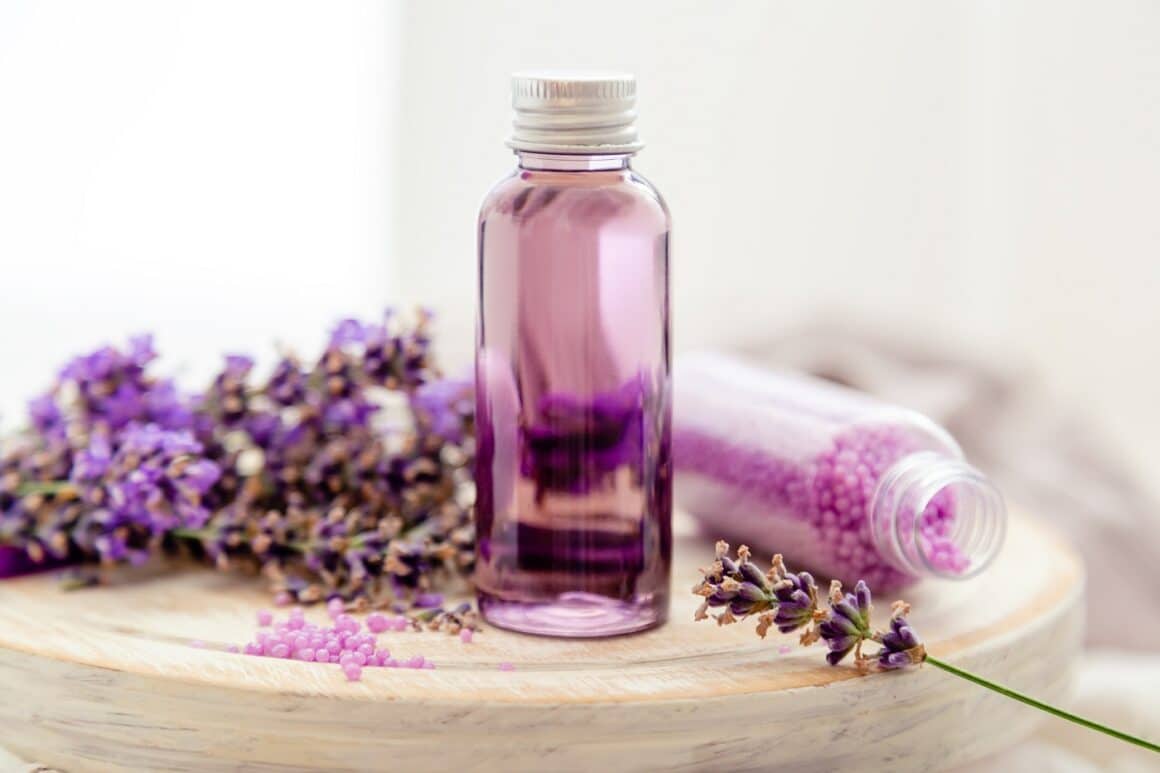 Lavender liquid. Bath cosmetics products in bottles on white wooden rustic board, fresh lavender flowers, soap, bath beads. Lavender essential oil, natural spa products. Aromatherapy treatment.