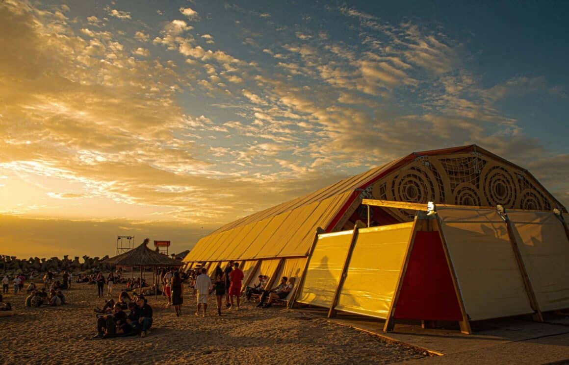 cort de festival amplasat pe plaja si tineri care se relaxeaza peplaja la Sun Waves, de 1 Mai la mare