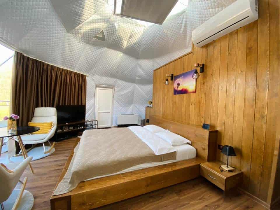 interiorul unui cort de glamping de lux, cu pat masiv si perete din lemn