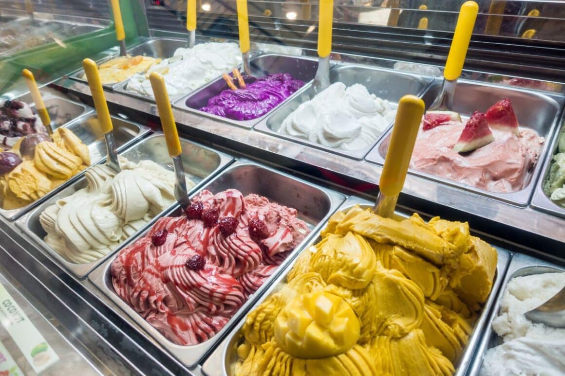 raftul unei gelaterii plin cu recipiente de ănghețată artizanală de diverse culori si arome