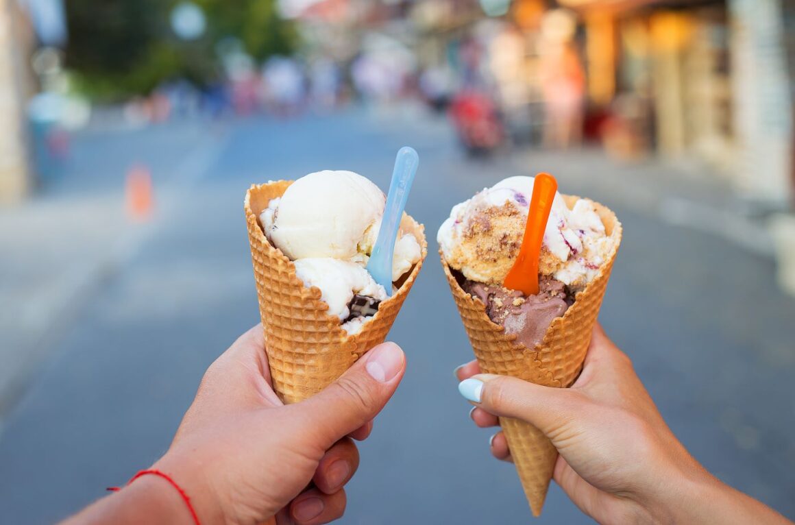 două conuri cu înghețatî artizanală ținute in mana de cineva, iar in fundal strada blurrata