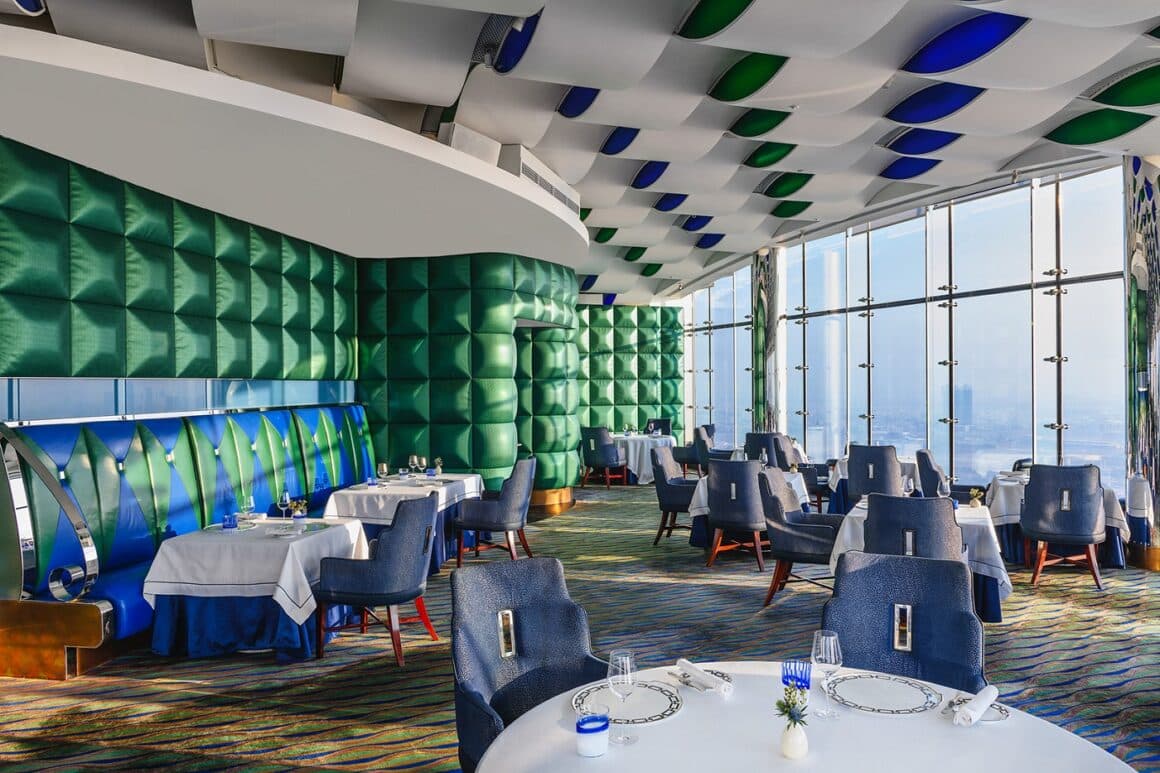 Restaurantul Al Muntaha din Dubai, cu mese elegante, fotolii tapitate, un perete din geamuri si altul capitonat cu material verde