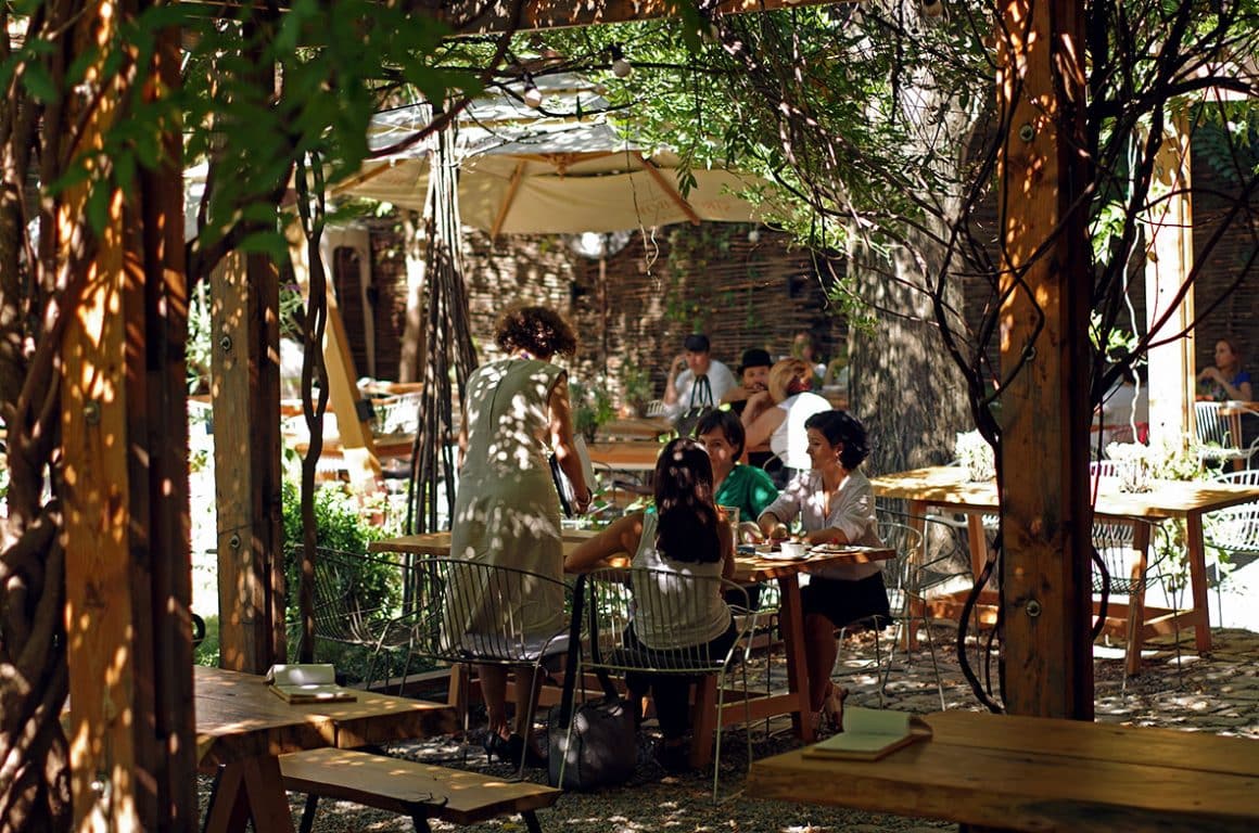 oameni care iau masa la Cafe Verona pe terasa umbrita de copaci si umvrele