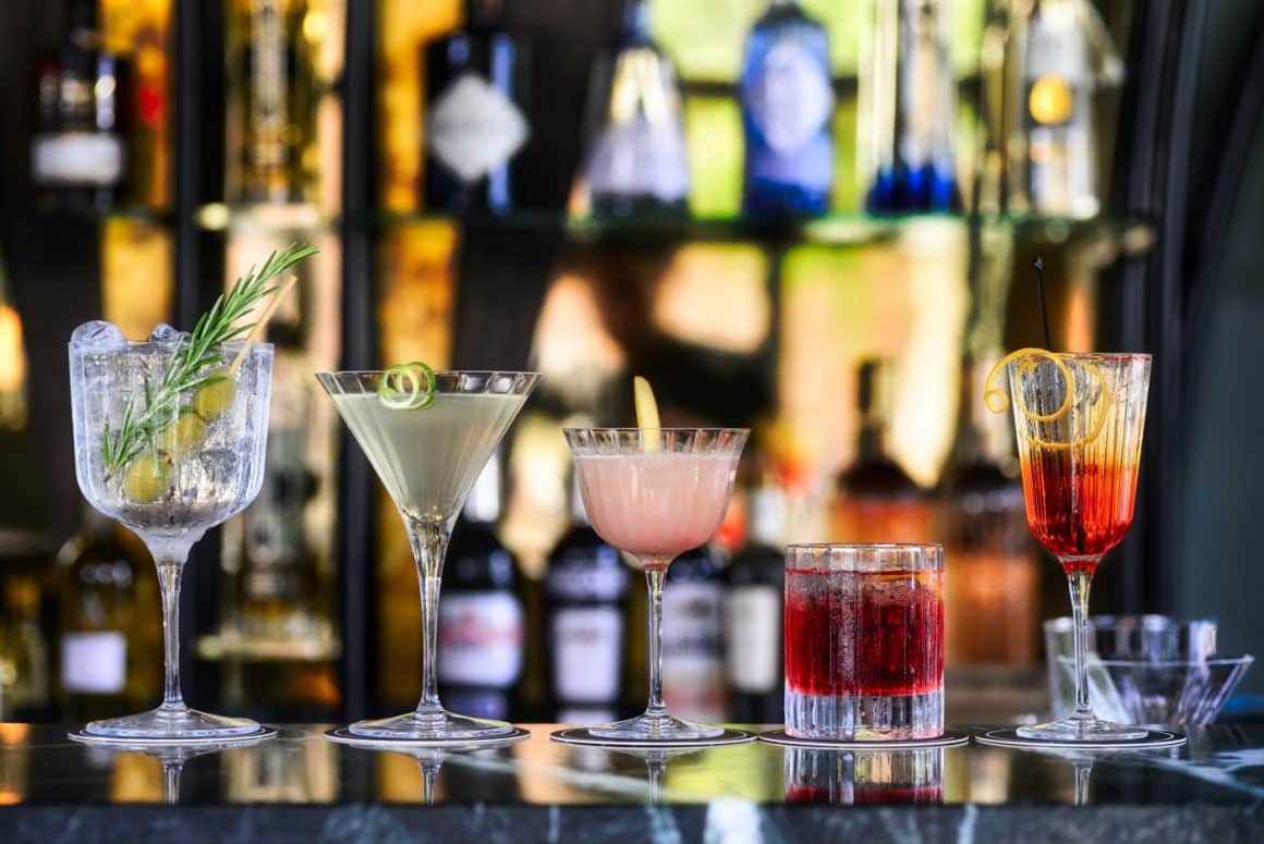 mai multe pahare cu cocktailuri colorate sunt puse pe tejgheaua unui bar. 