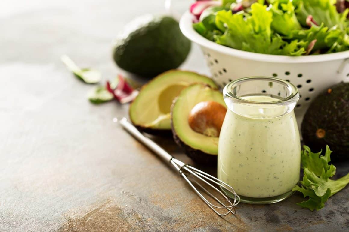 Dressinguri pentru salate: avocado ranch intr-un borcan mic alaturi de o strecuratoare cu frunze de salata si avocado