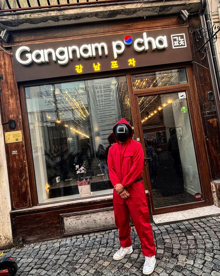 Intrarea in restaurant Gangam Pocha si o persoana costumata cu un costum roșu ca în Aquid Game. Locuri noi în București
