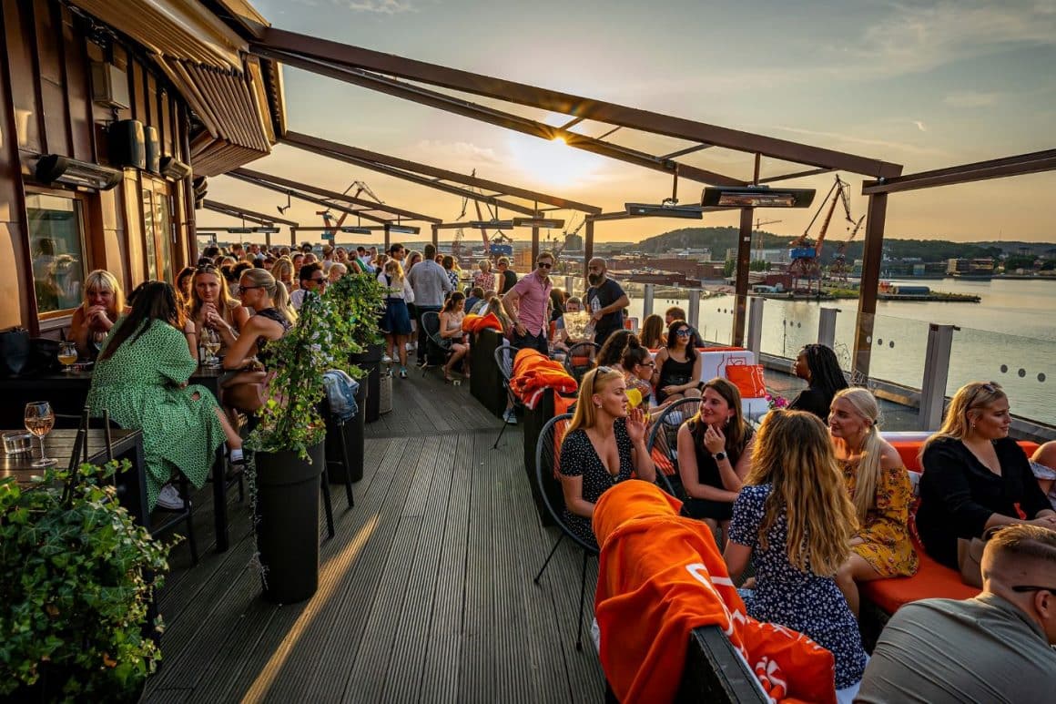 mai multi tineri stau la mese si socializeaza pe terasa unui sky bar