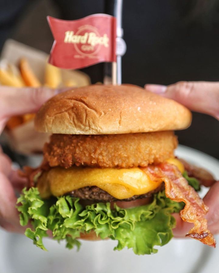Original Legendary Burger de la Hard Rock Cafe, din vita Angus, cu bacon, cheddar si onion ring. Burgeri gustoși