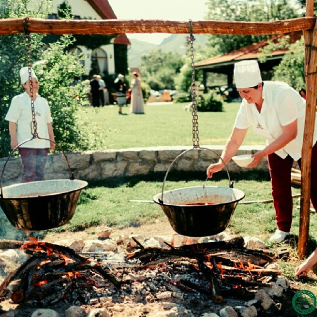 2 bucataresc gatesc in aer liber, la 2 tuciuri imense, atarnate de o barna de lemn deasupra focului. Restaurante de la sate, România culinară tradițională