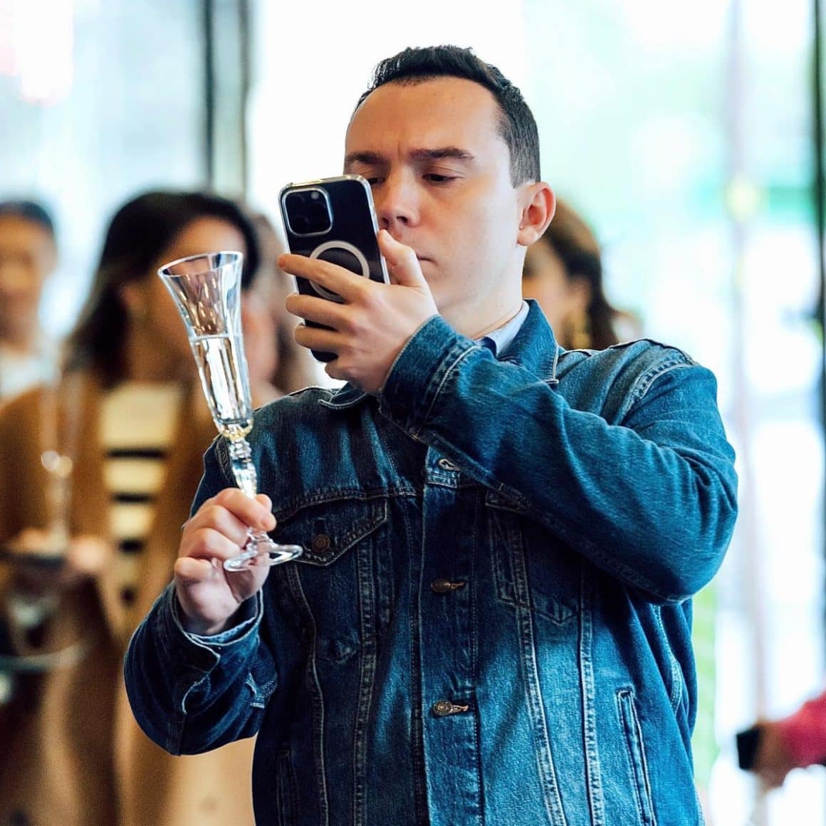 Catalin de la FoodInRomania fotografiaza cu telefonul un pahar de sampanie pe care-l tine in mana