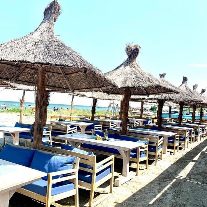 mese cu bancute asezate sub umbrele de paie, pe plaja, la Cherhana Pontica