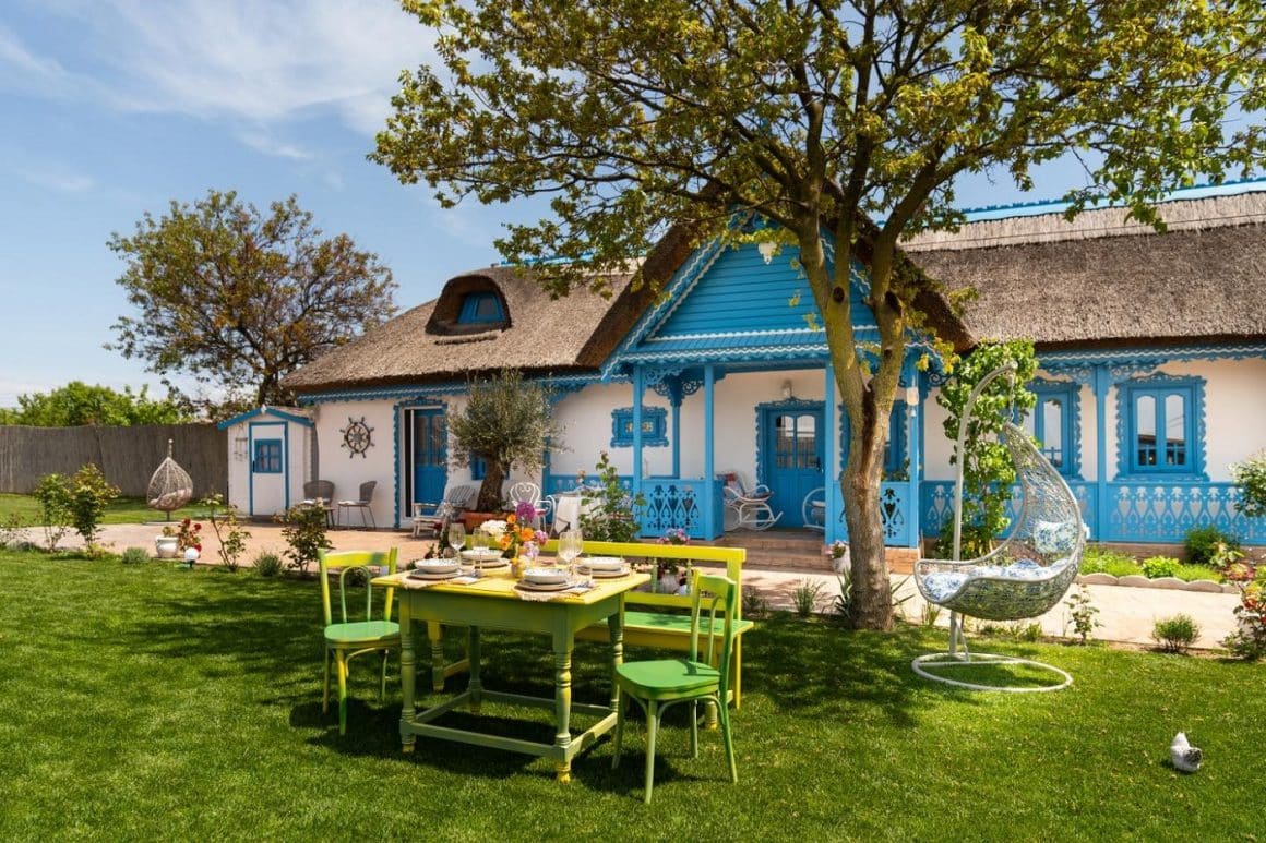 Casa Ilinca din Jurilovca, cu ferestre si pridvor vopsite albastru si o curte cu gazon pe care e asezata o masă de lemn. Unde măncăm în Delta Dunării