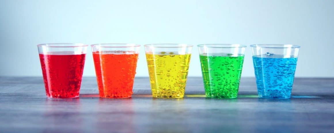 cinci pahare de plastic cu sucuri de diferite culori pe un fundal gri