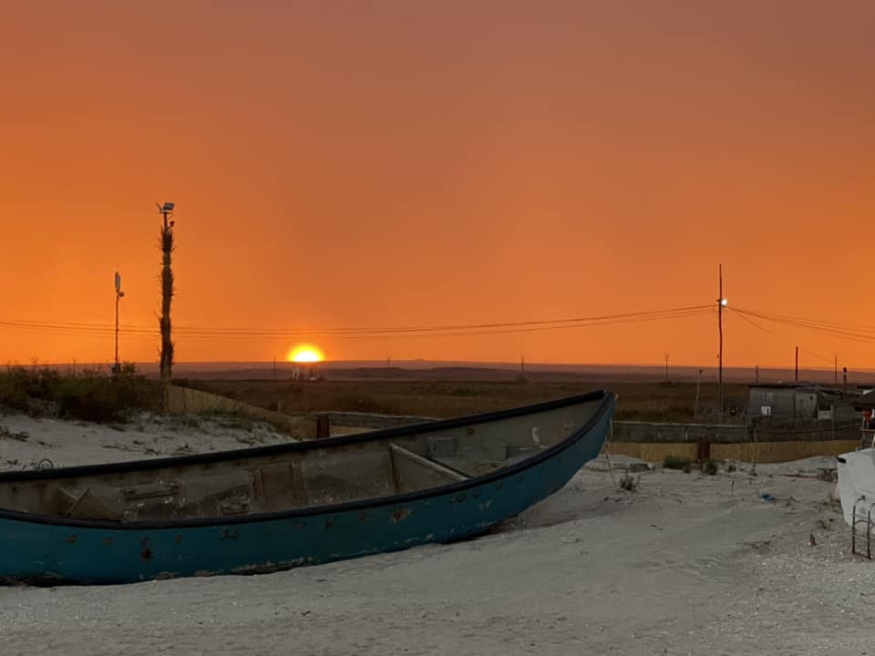 barca trasa pe plaja, fotografiata la asfintit, cu soarele care apune in fundal