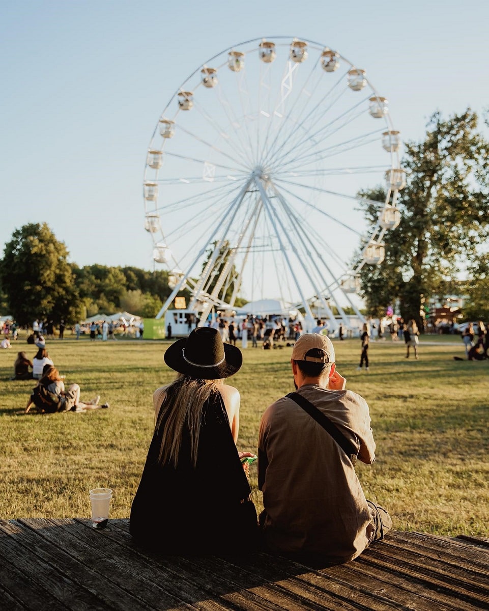 Oameni se relaxează pe iarbă la Electric Castle 2023, in fata rotii mari de festival