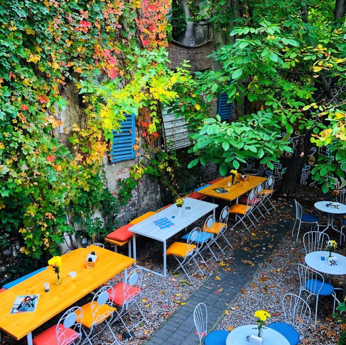 Mese colorate asezate in curtea Arome, cu o casa acoperita de iedera. Grădini din București