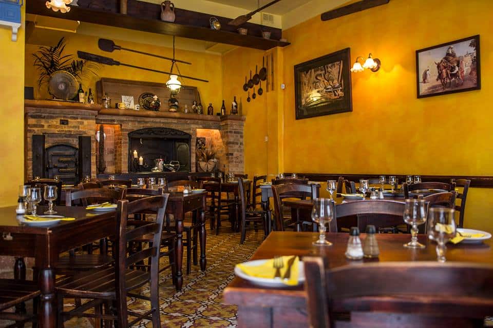 interiorul restaurantului Ta` Kris din Malta, cu pereti galbeni și mai multe  mese de lemn  pe care sunt asezate pahare de sticla