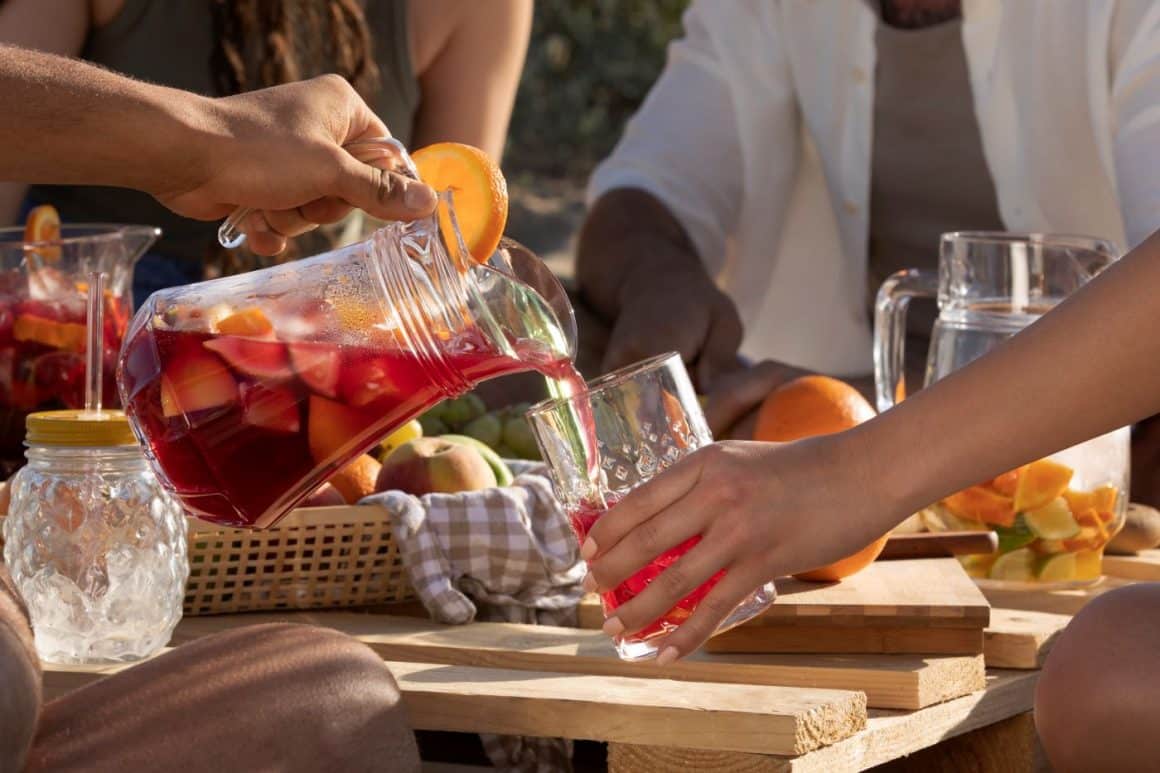 mai mulți tineri beau sangria în  din pahare în aer liber pe o masă rustică unde sunt fructe