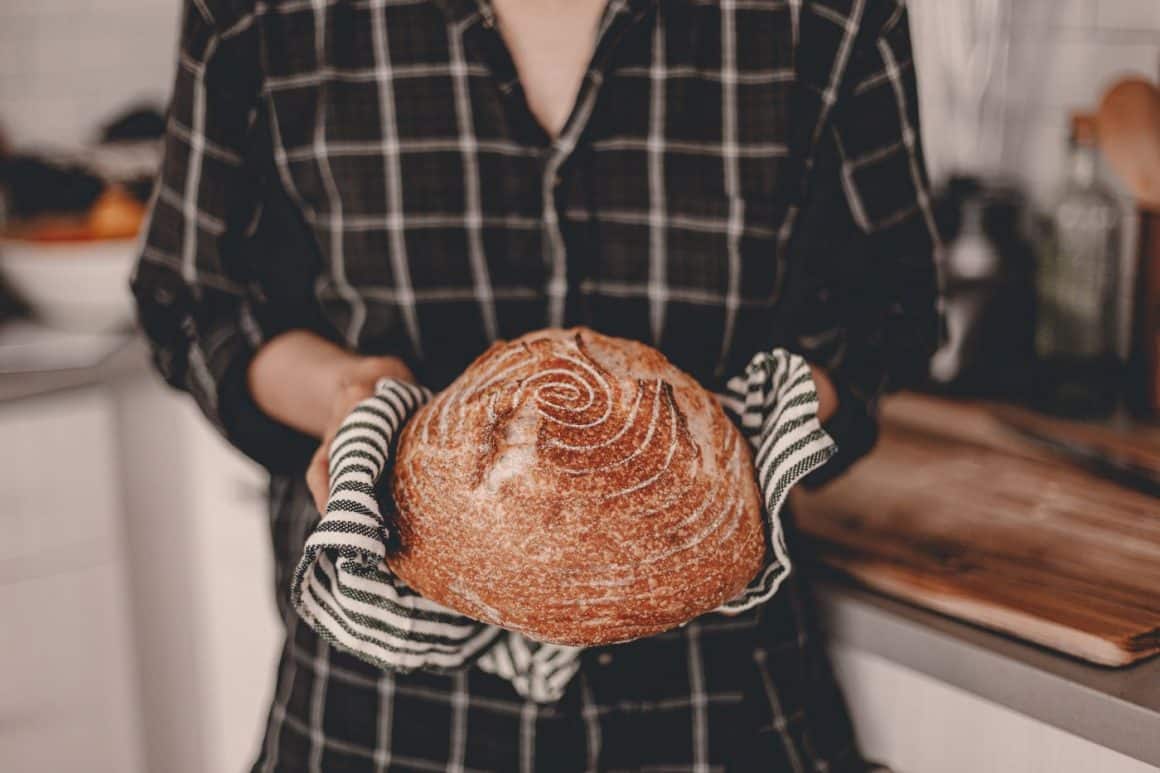 o femeie tine in maine, cu ajutorl unui servet, o paine proaspata cu maia scoasa din cuptor