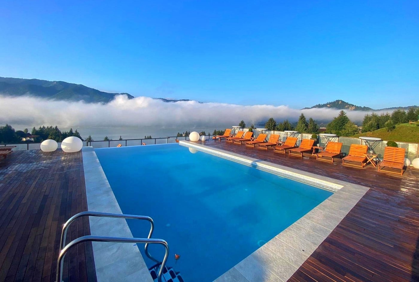 piscina infinity cu sezlonguri portocalii si vedere panoramica spre muntii acoperiti de nori la Panoramic Colibita