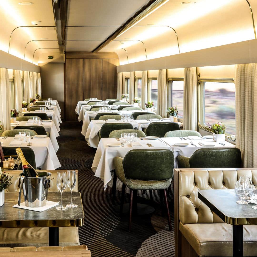 salonul de luat masa  dintr-un tren, cu scaune tapitate verde si fete de masa albe. trenuri internaționale de lux