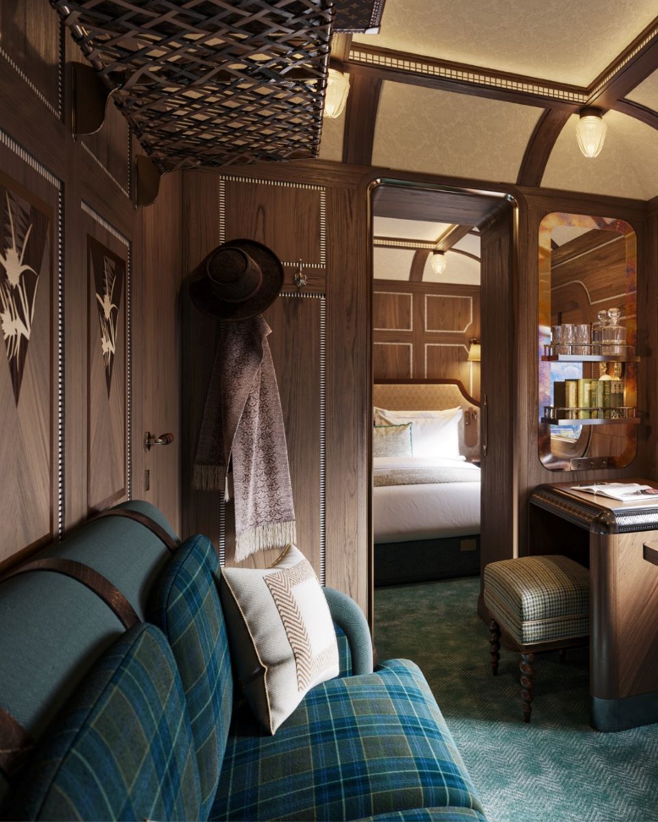 un salon de călătorit dintr-un vagon de trenuri internaționale de lux, cu un ziar și o lampă pusa pe masa din fata unei canapele confortabile. 